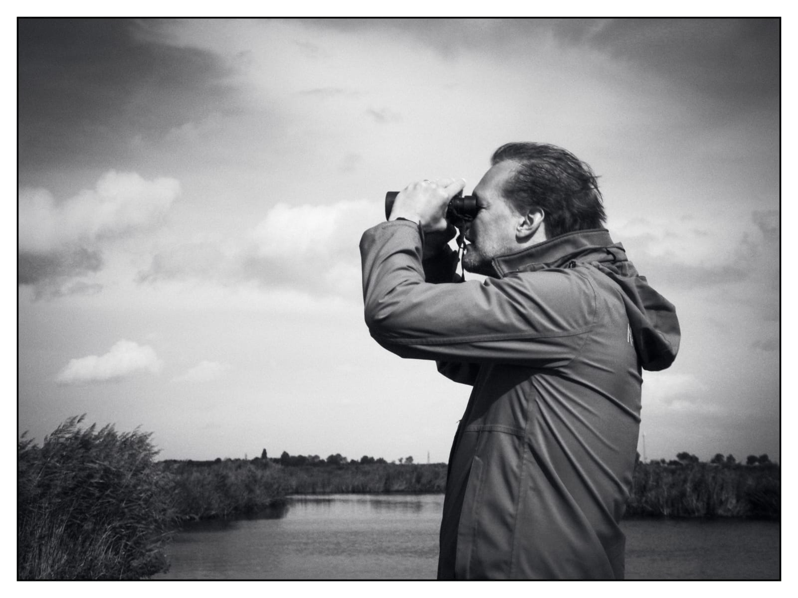 Klaas kijkt met een verrekijker over het water en riet in het Ilperveld